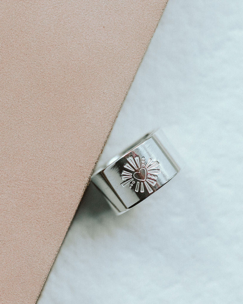 Silver ring with a darling heart design on a light pink and white background
