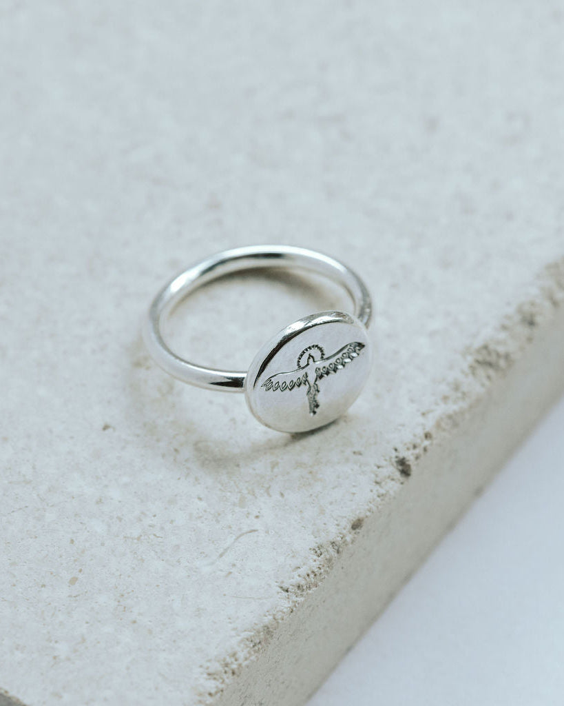Silver ring with hand stamped phoenix design on a textured stone surface