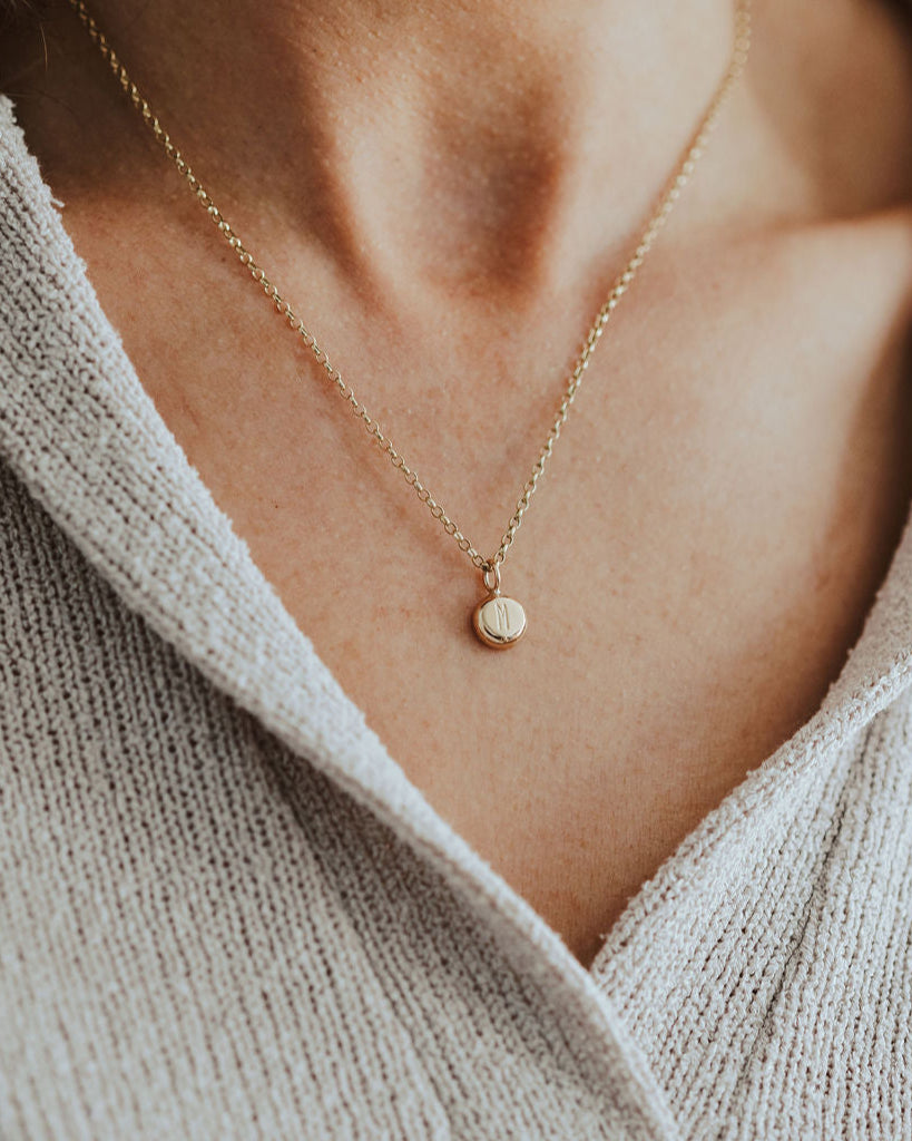 Necklace with a small pendant worn by a person in a light-colored sweater.