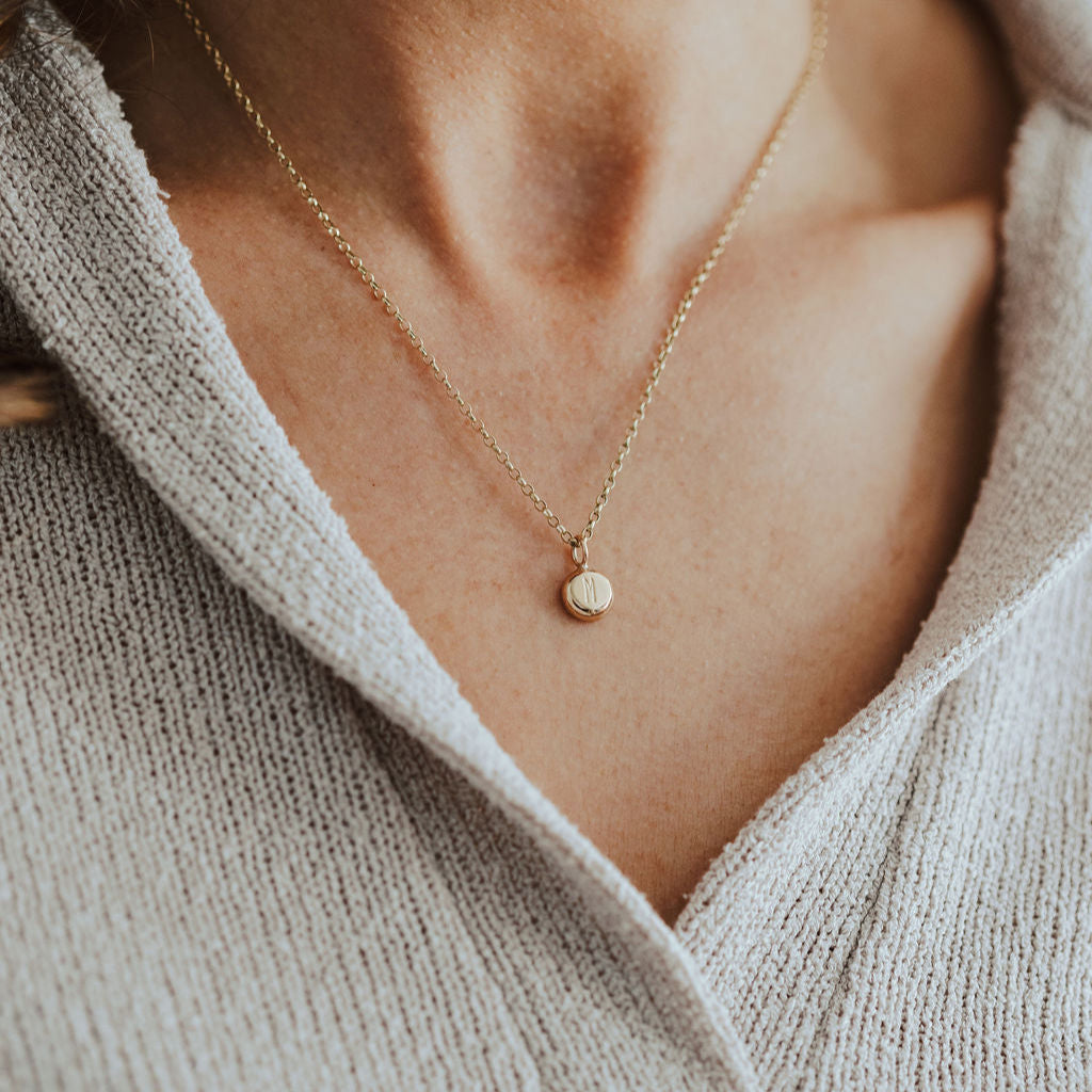 Necklace with a small pendant worn by a person in a light-colored sweater.