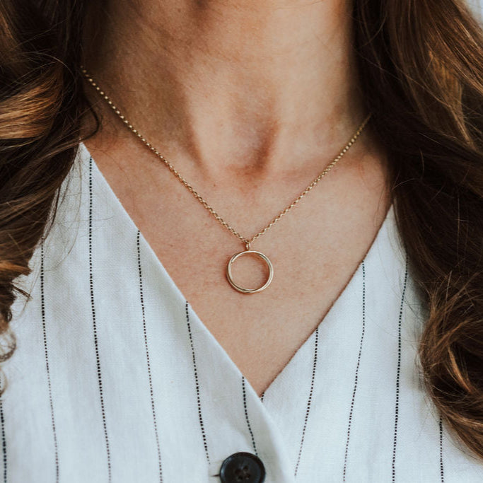 Person wearing a gold open circle necklace and a white and black striped top.