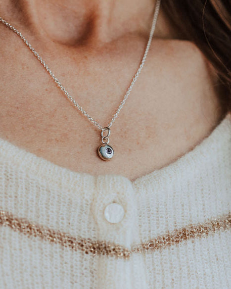 Close-up of a person wearing a necklace with a small birthstone pendant, against a neutral background.