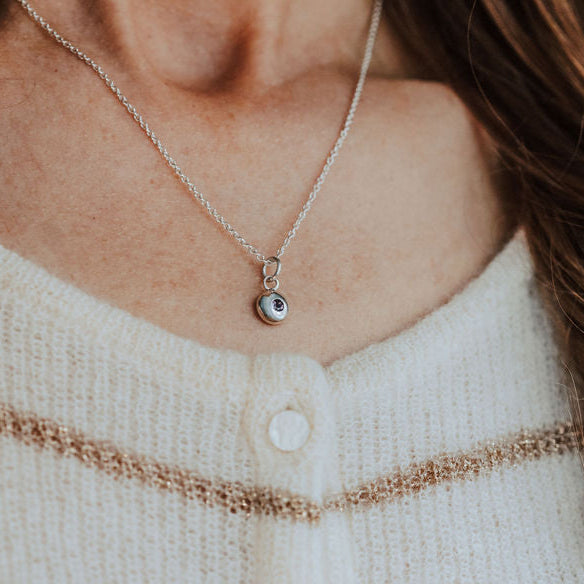 Close-up of a person wearing a necklace with a small birthstone pendant, against a neutral background.