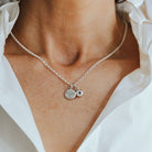Necklace with birthstone and phoenix pendants worn by a person in a white shirt.