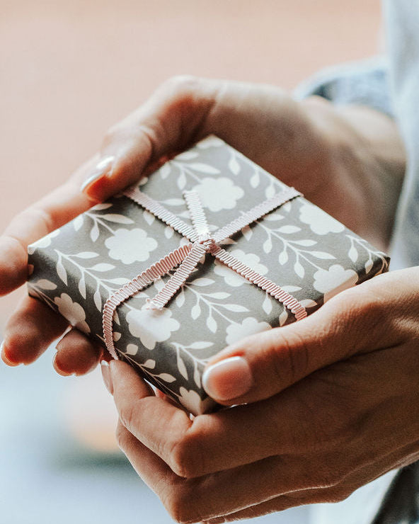 Present wrapped in black and white gift wrap with pink ribbon, held by womans hands