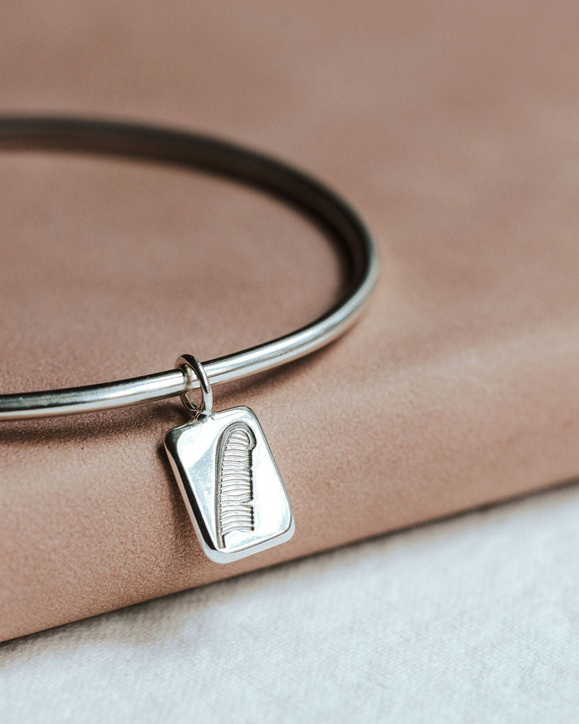 Silver bangle with a feather charm resting on a pink book.