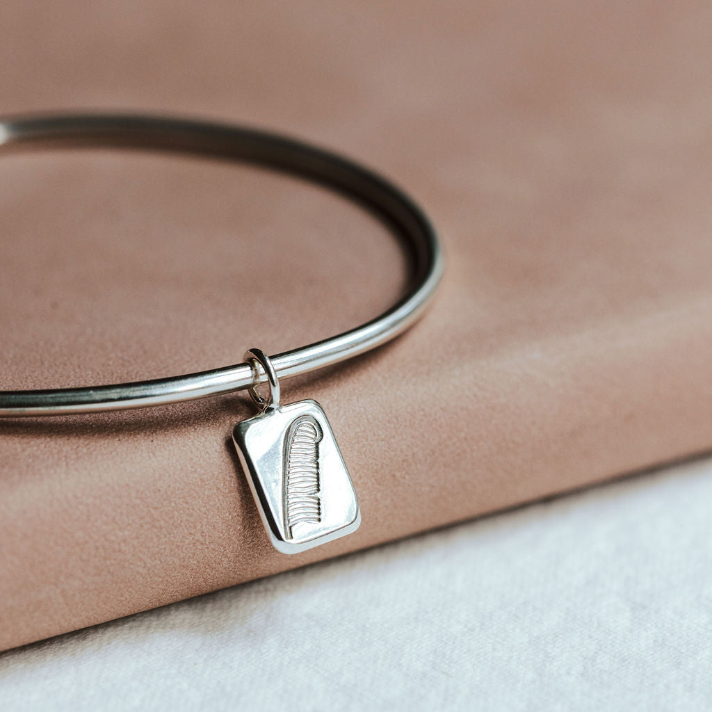 Silver bangle with a feather charm resting on a pink book.
