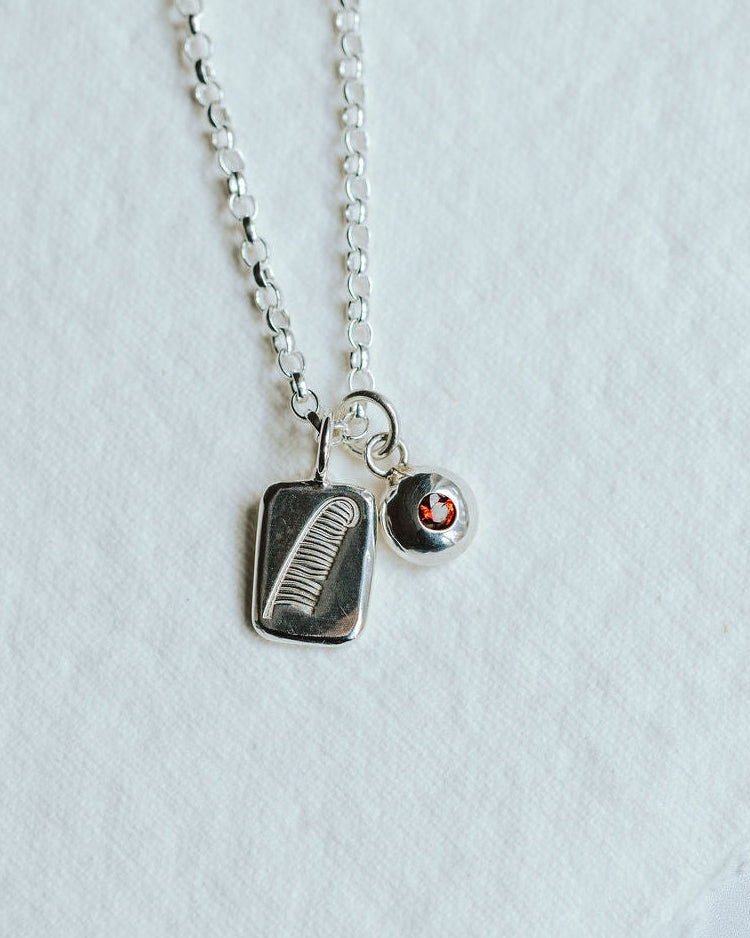 Necklace featuring two charms on a white background. One charm has a feather motif and one has a birthstone set in it.