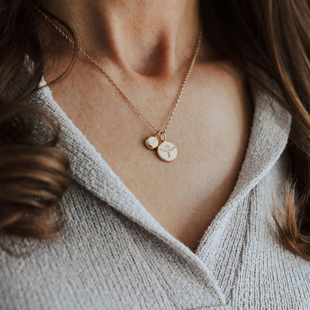 Close-up of a person wearing a delicate gold necklace with initial and phoenix pendants.