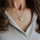 Close-up of a person wearing a delicate gold necklace with initial and phoenix pendants.