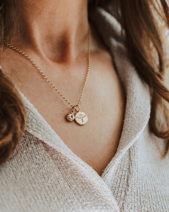 Close-up of a person wearing a delicate gold necklace with Phoenix and birthstone pendants.