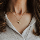 Close-up of a person wearing a gold necklace with phoenix and initial pendants.
