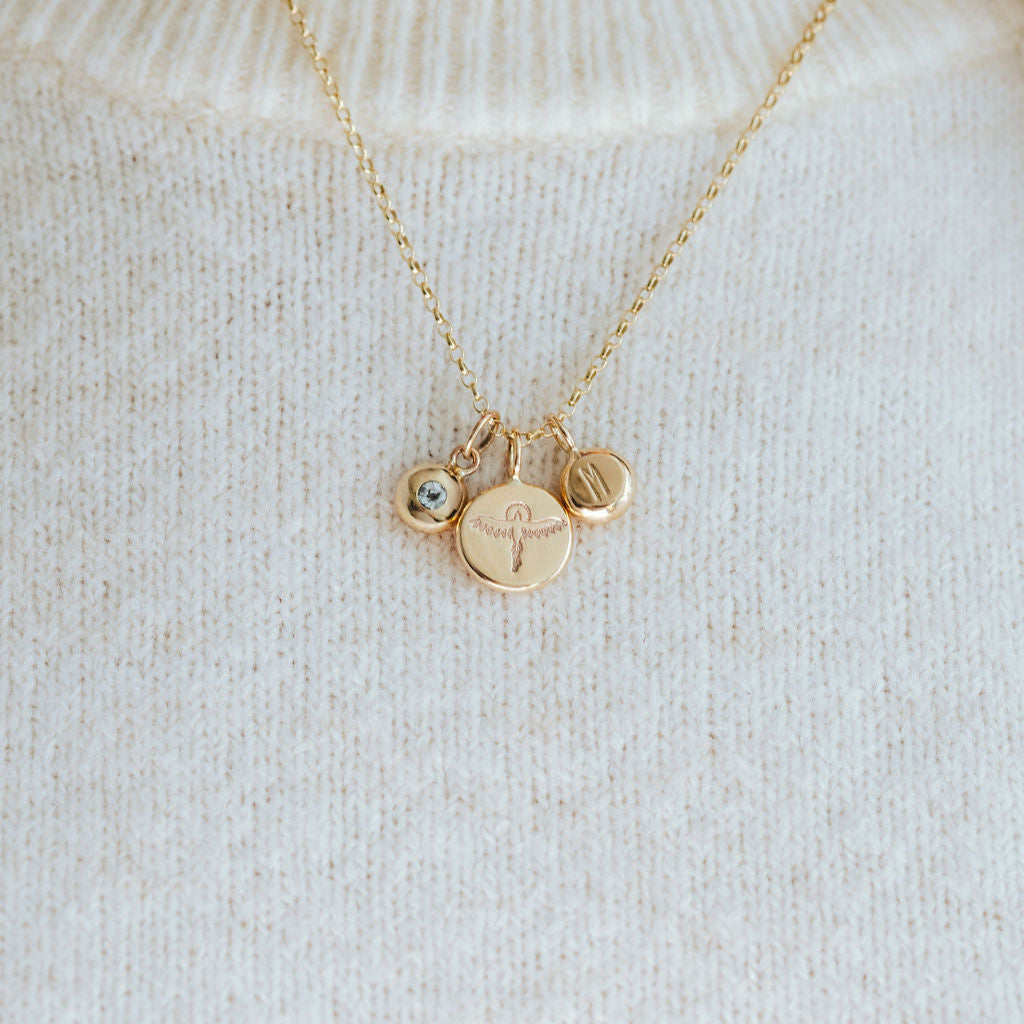 Gold necklace with phoenix, birthstone and initial pendants on a white sweater