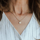 Woman wearing solid gold tree bark textured necklace and white v neck shirt.