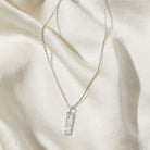 Silver necklace with a rectangular bark textured pendant on a beige fabric background