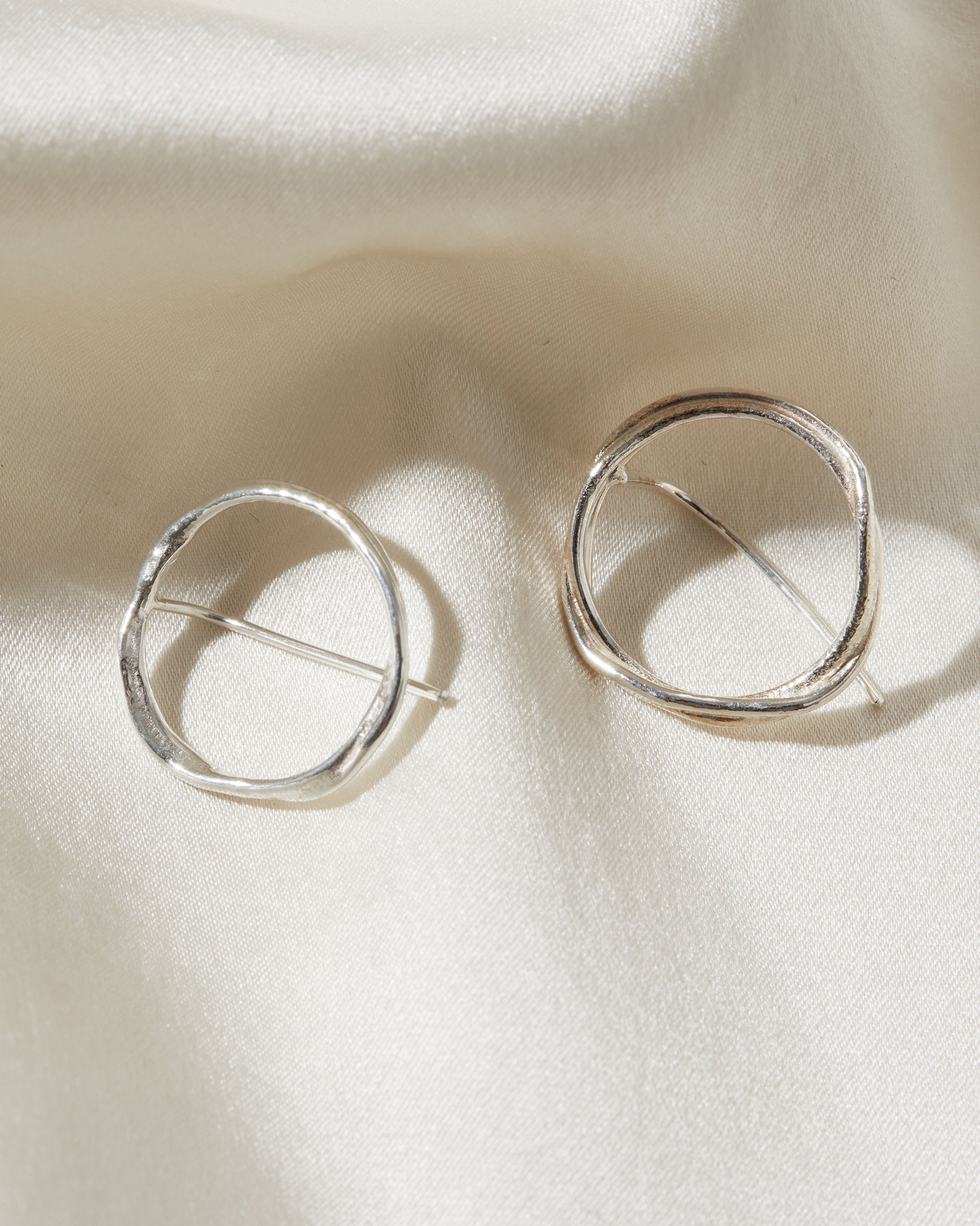 Silver circular earrings on a beige fabric background