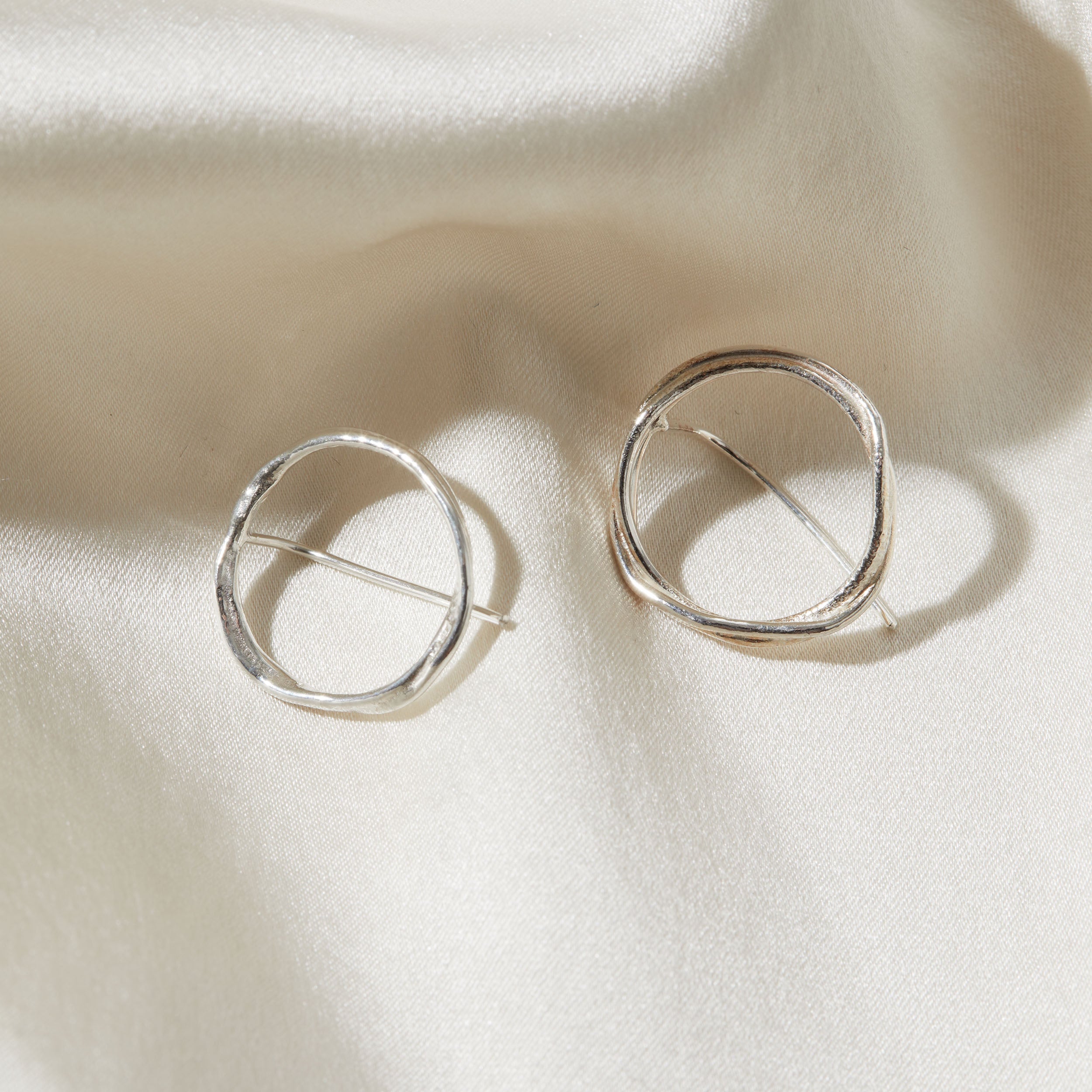 Silver circular earrings on a beige fabric background