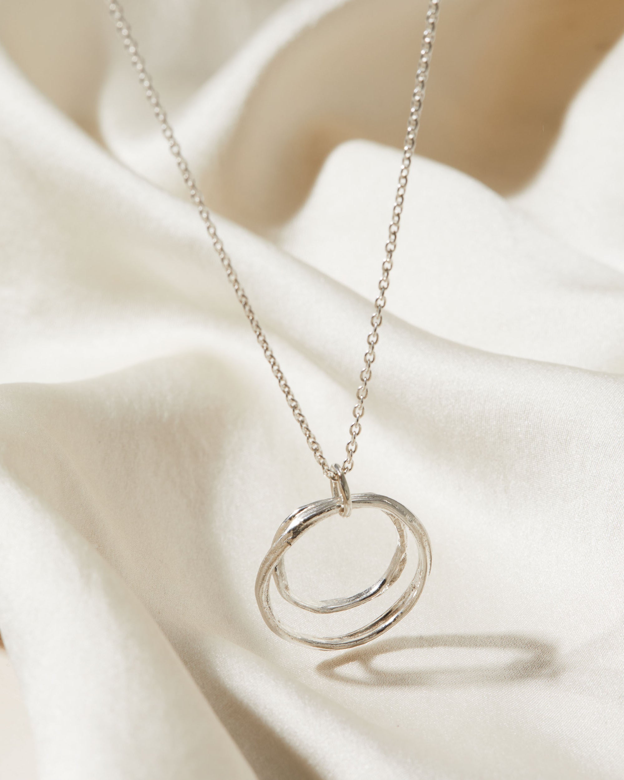 Silver necklace with a double-circle pendant on a soft beige fabric background