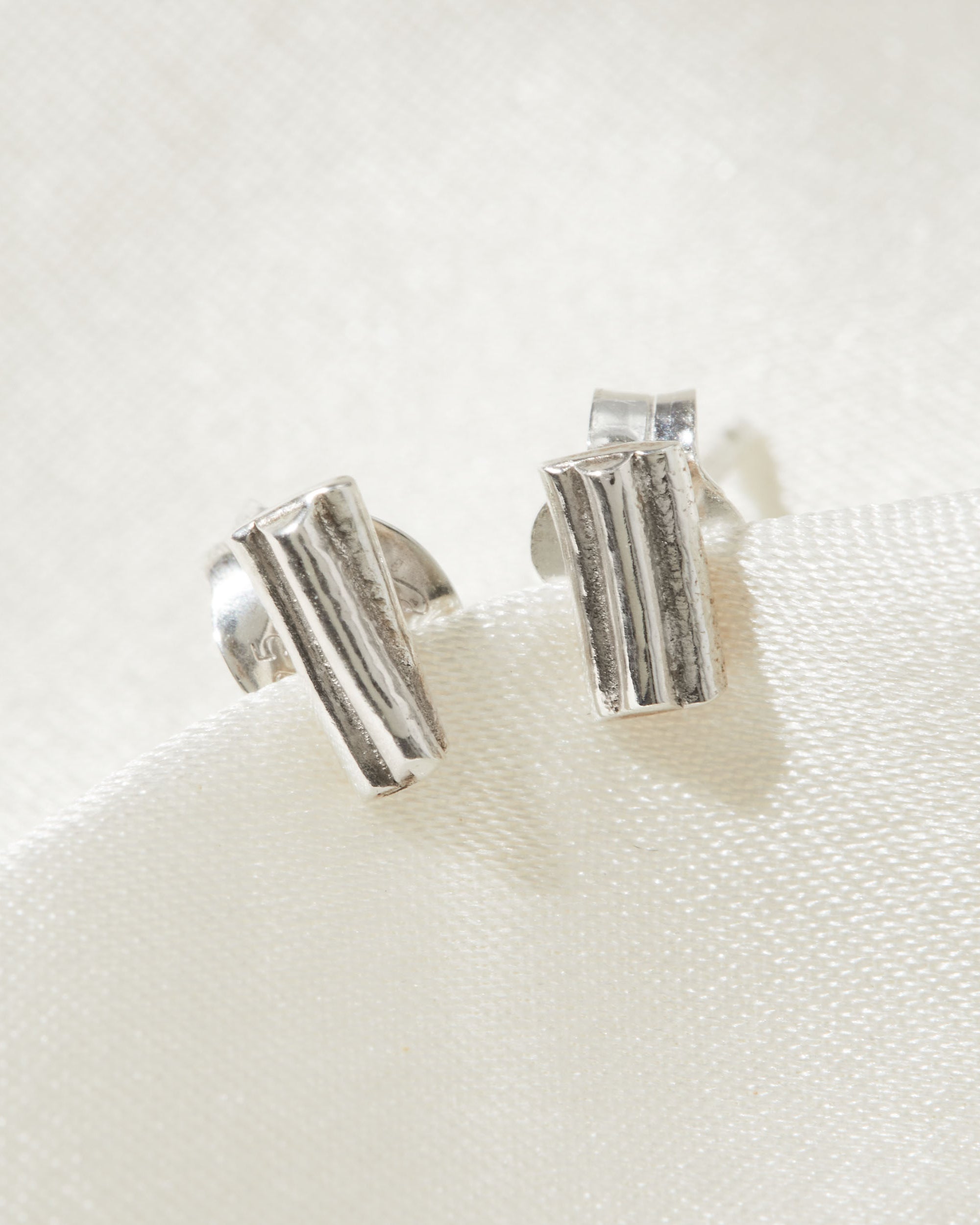 Silver ripple stud earrings on a white fabric background