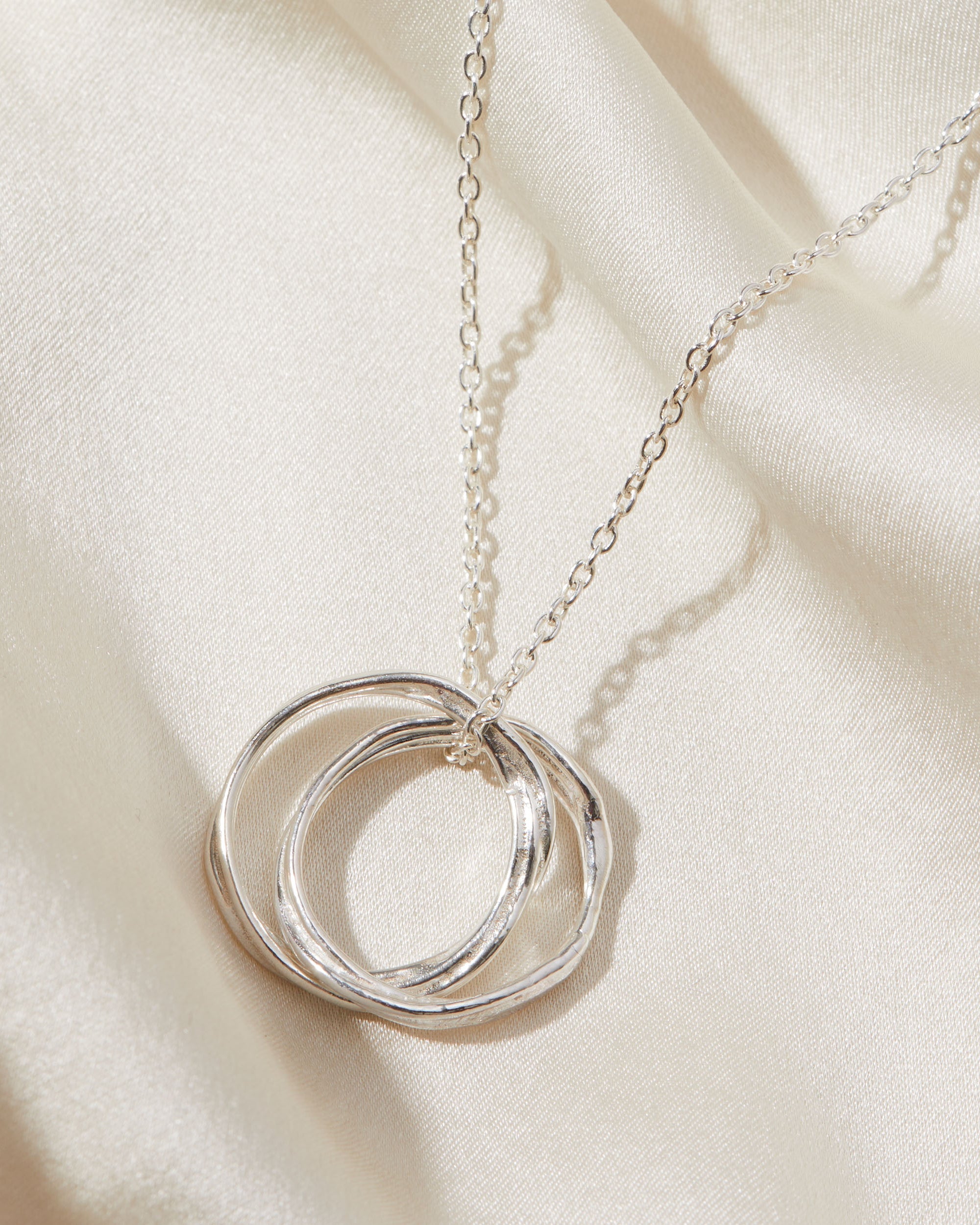 Silver necklace with a double circular pendant on a beige fabric background