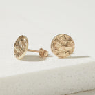 Gold round bark textured stud earrings on a light background