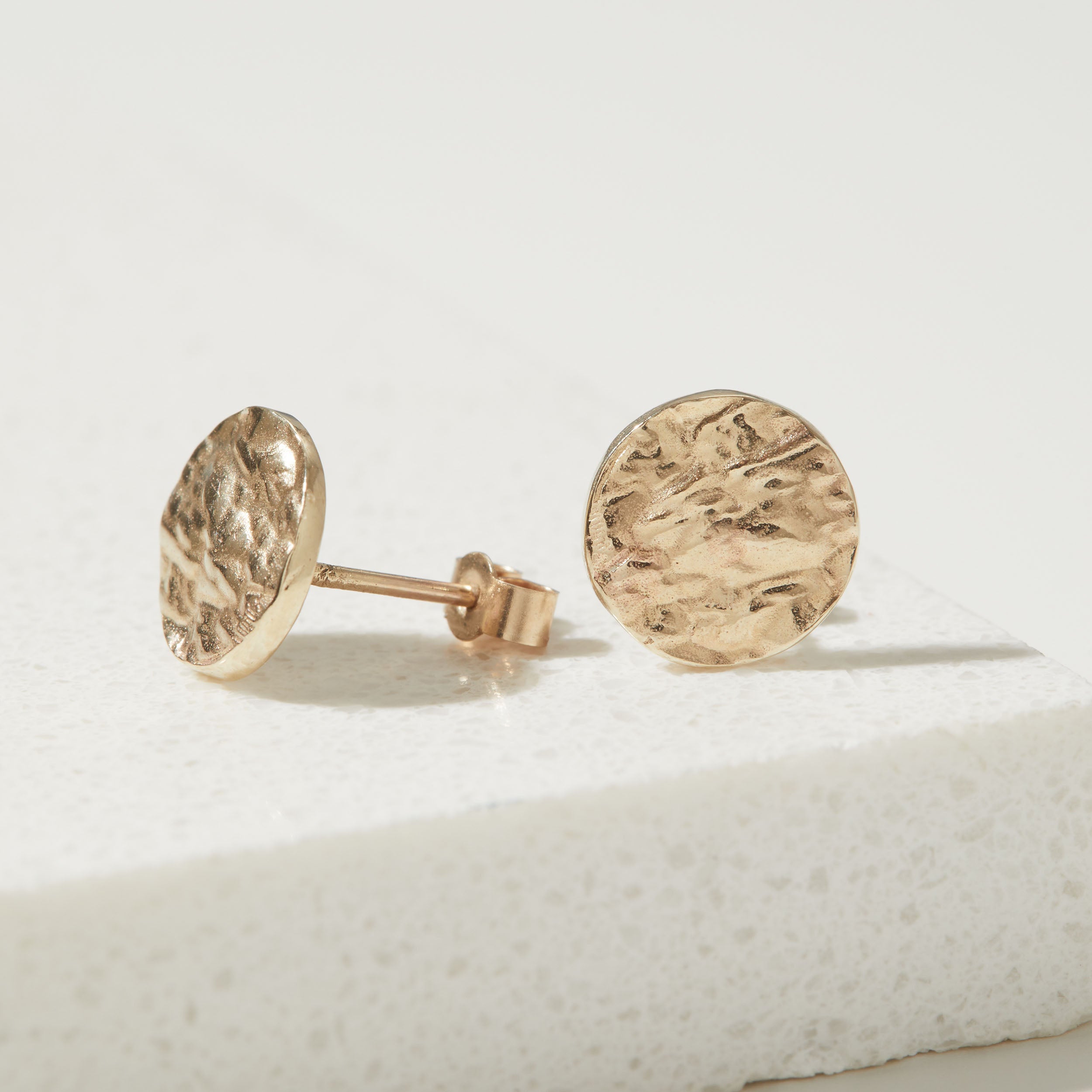 Gold round bark textured stud earrings on a light background