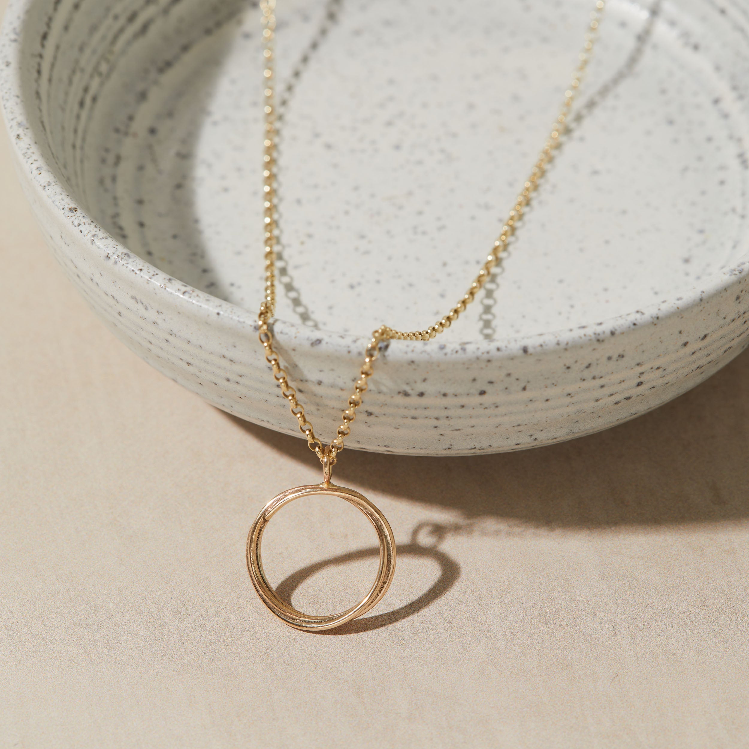 Gold necklace with a circular pendant on a neutral background