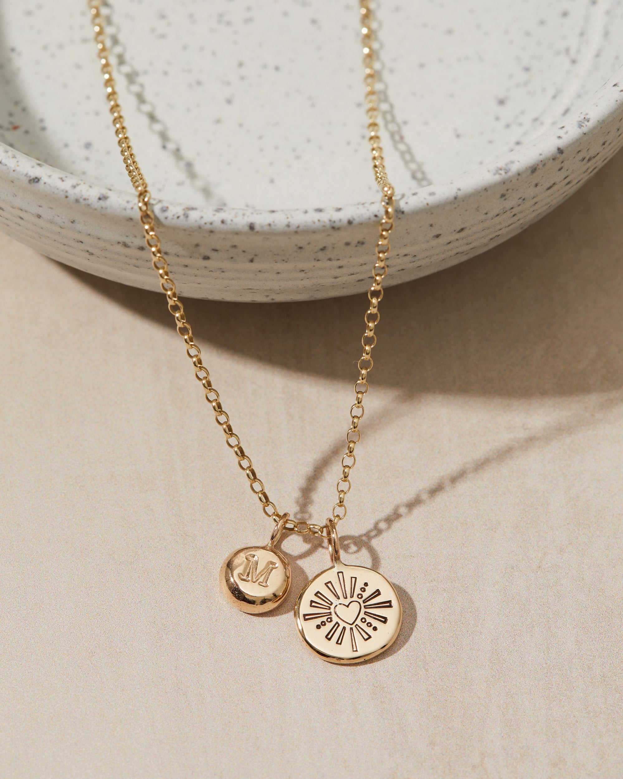 Gold necklace with initial and heart pendants on a neutral background