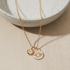 Gold necklace with initial and heart pendants on a neutral background