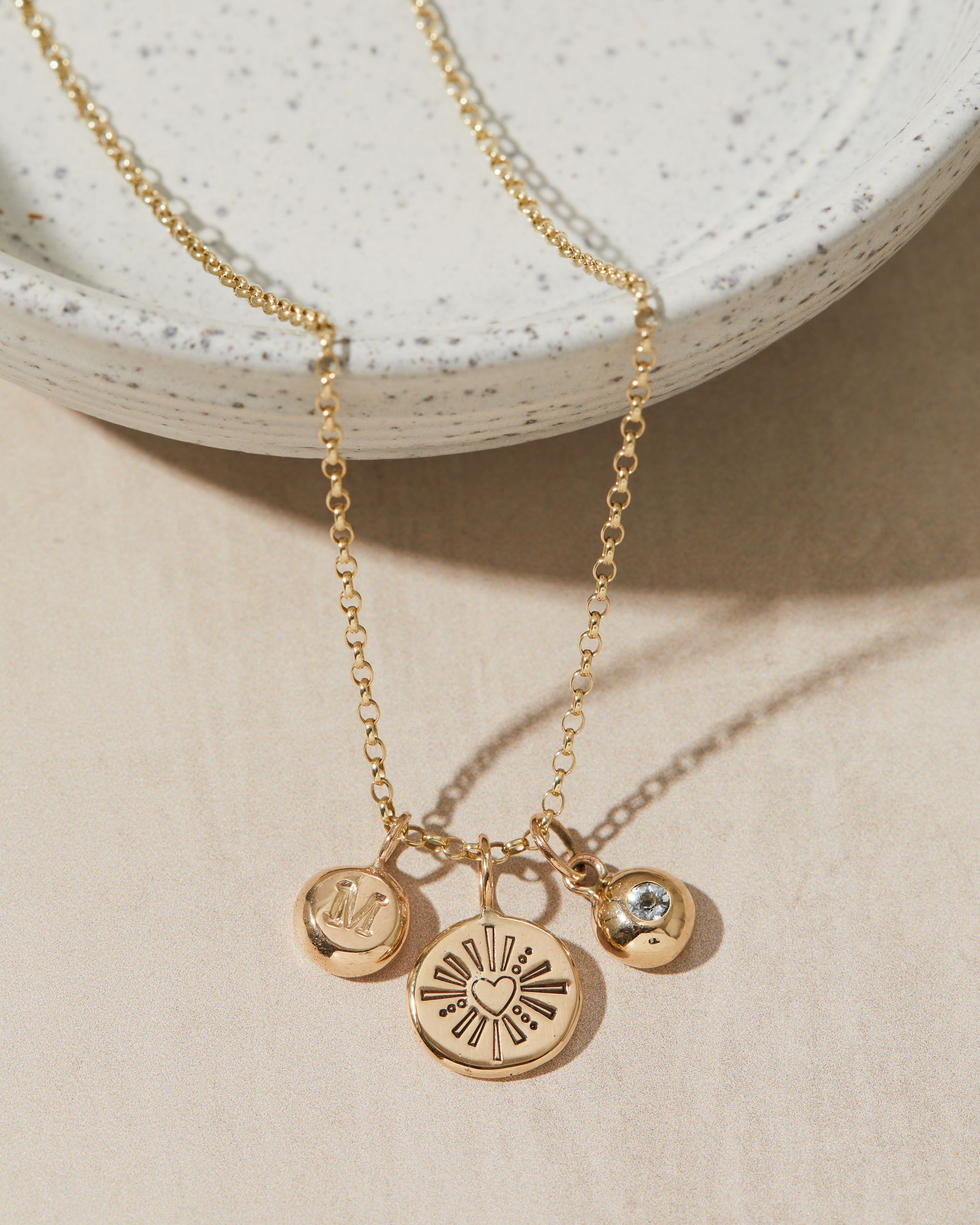 Gold necklace with initial-birthstone-heart charms on a neutral background
