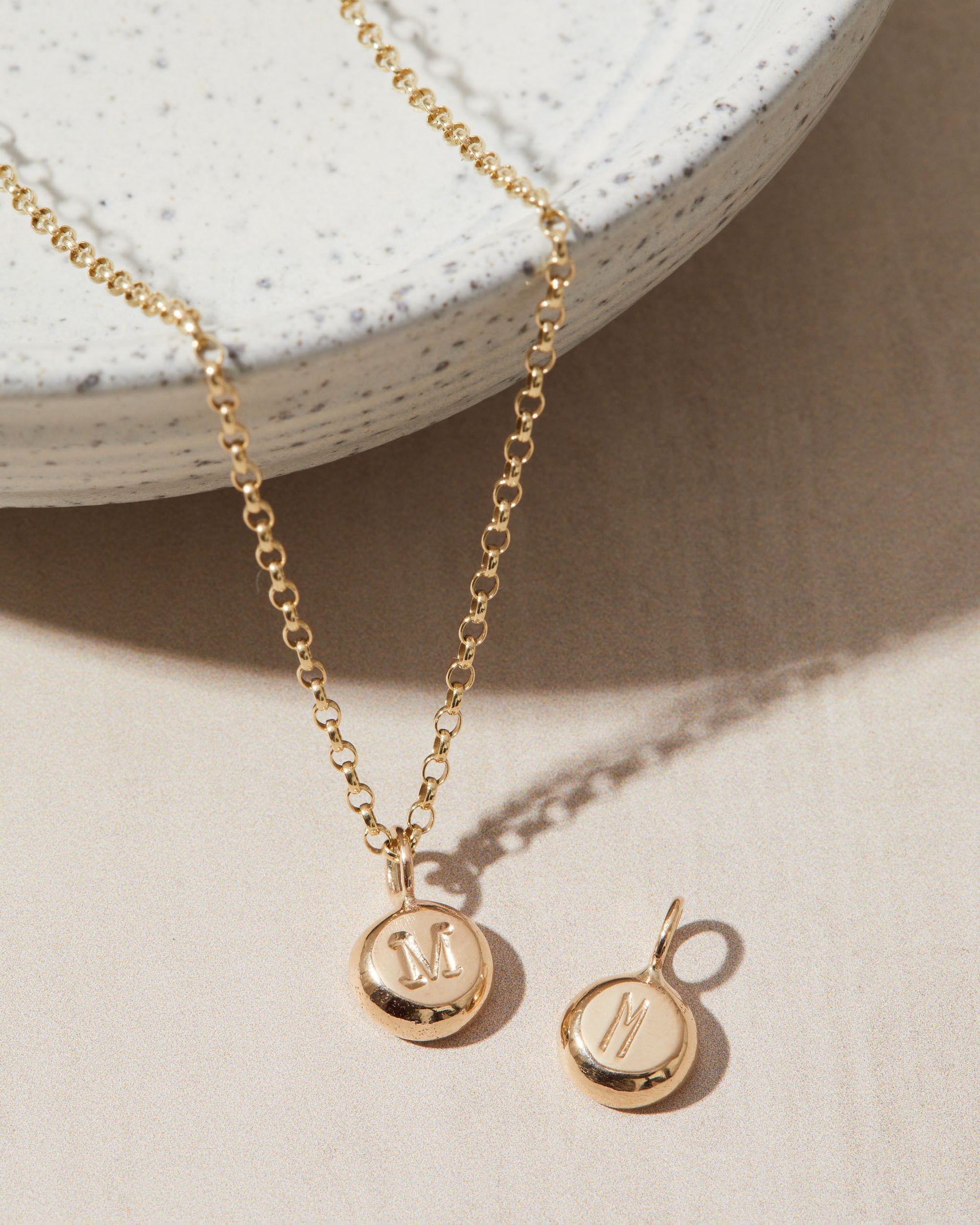 Gold necklace and pendant with 'M' charm on a neutral background