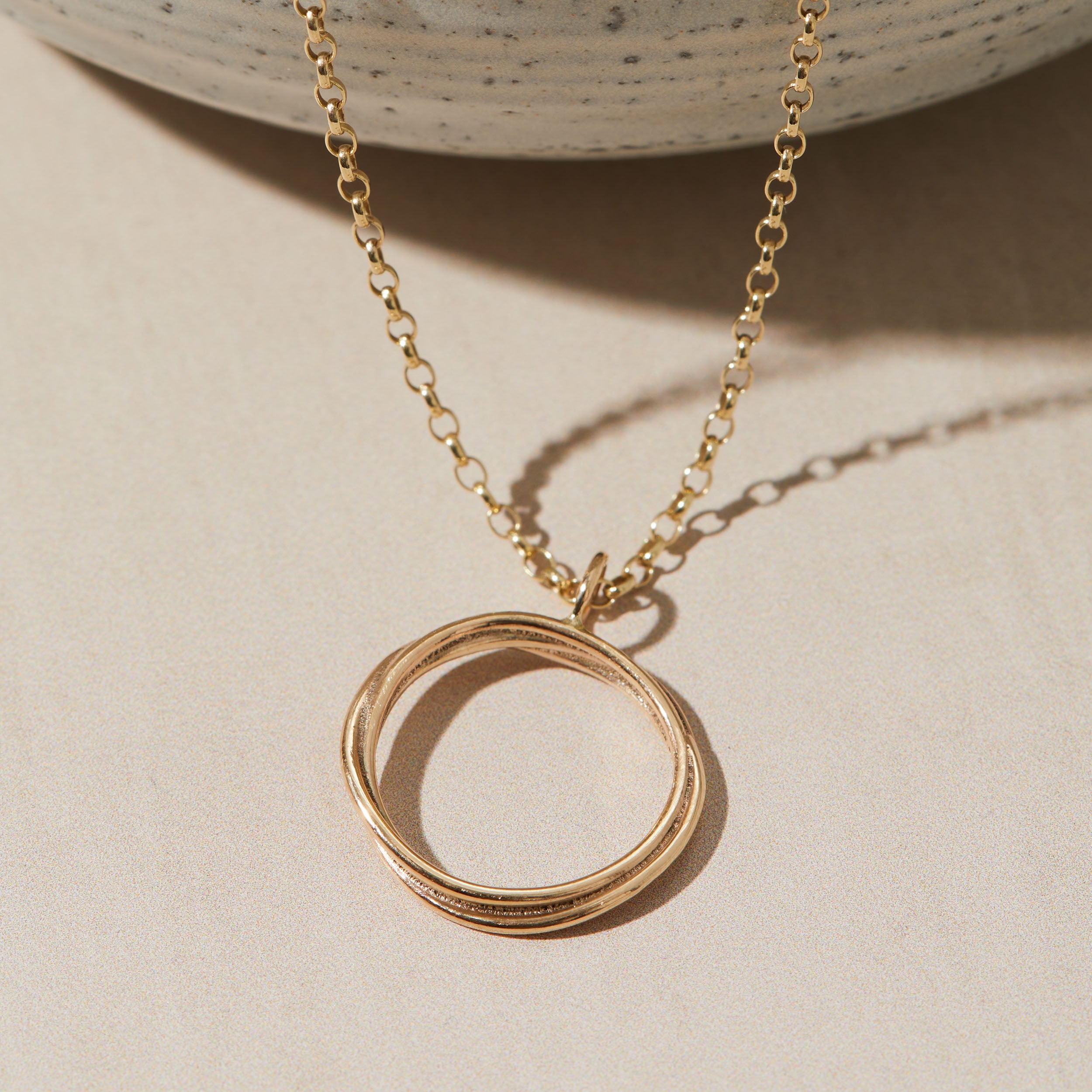 Gold necklace with a circular pendant on a beige background