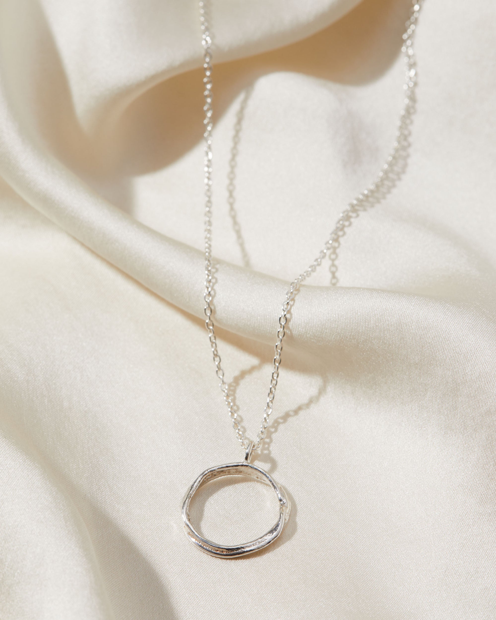 Silver necklace with a circular pendant on a soft beige fabric background
