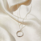 Silver necklace with a circular pendant on a soft beige fabric background