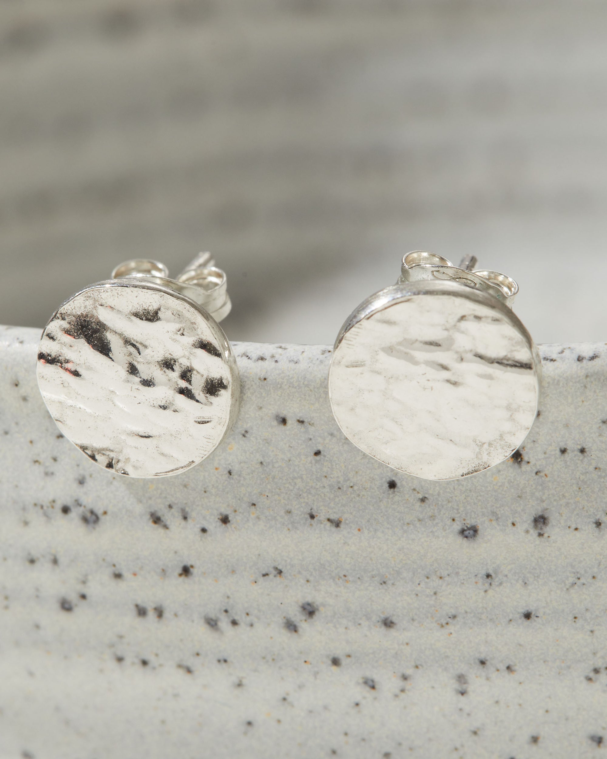 Silver round bark textured stud earrings on a speckled gray surface