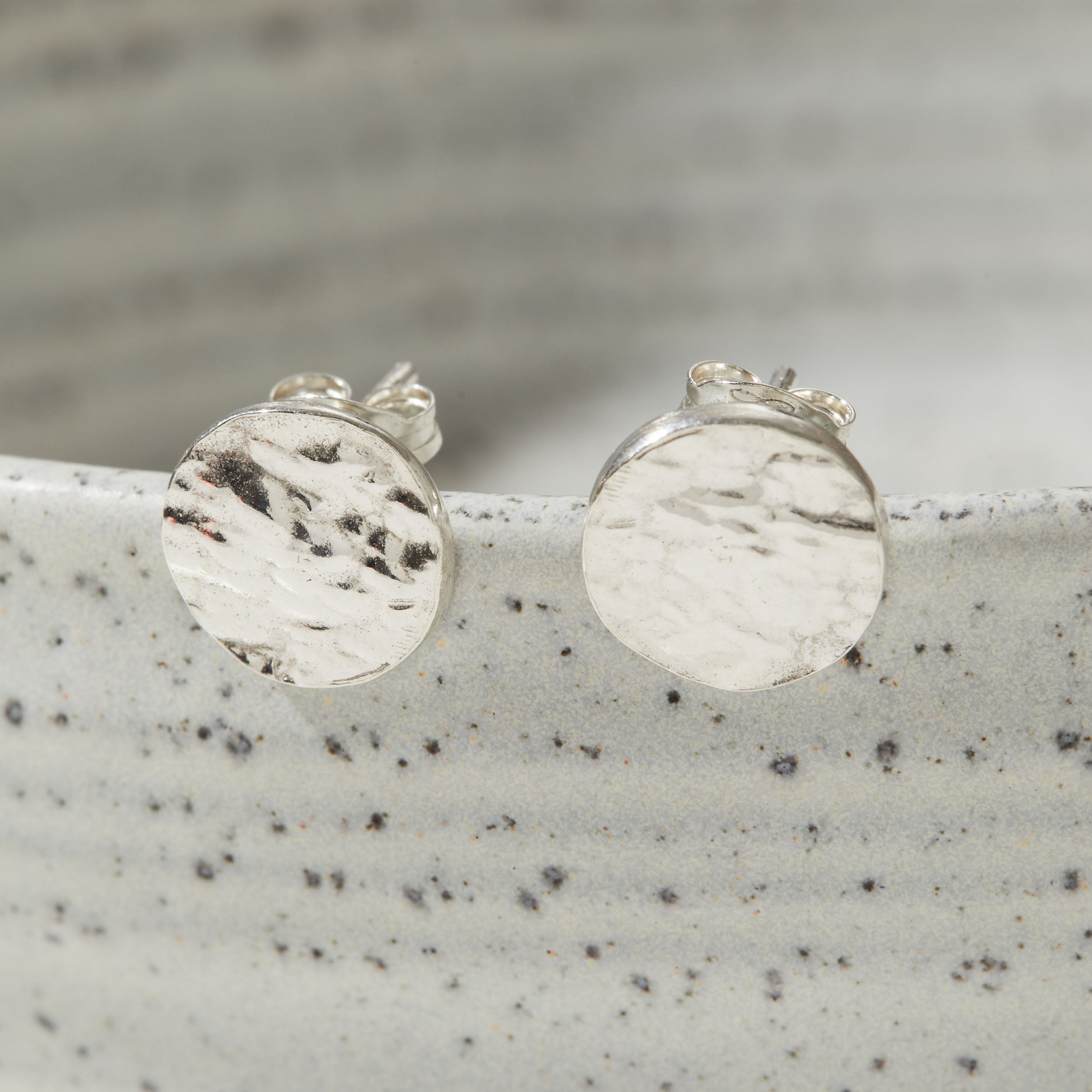 Silver round bark textured stud earrings on a speckled gray surface