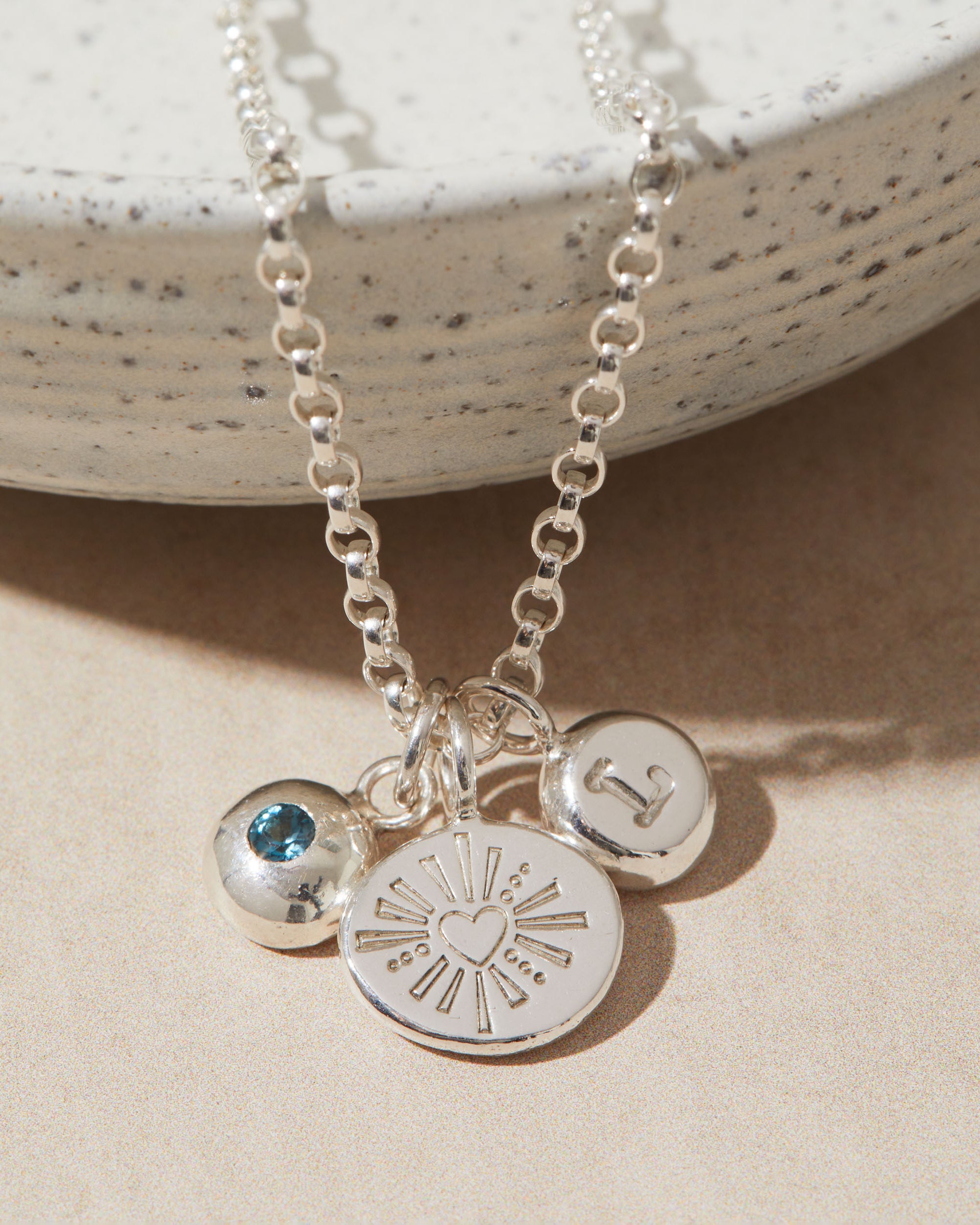 Silver necklace with heart, initial, birthstone charms on a beige surface