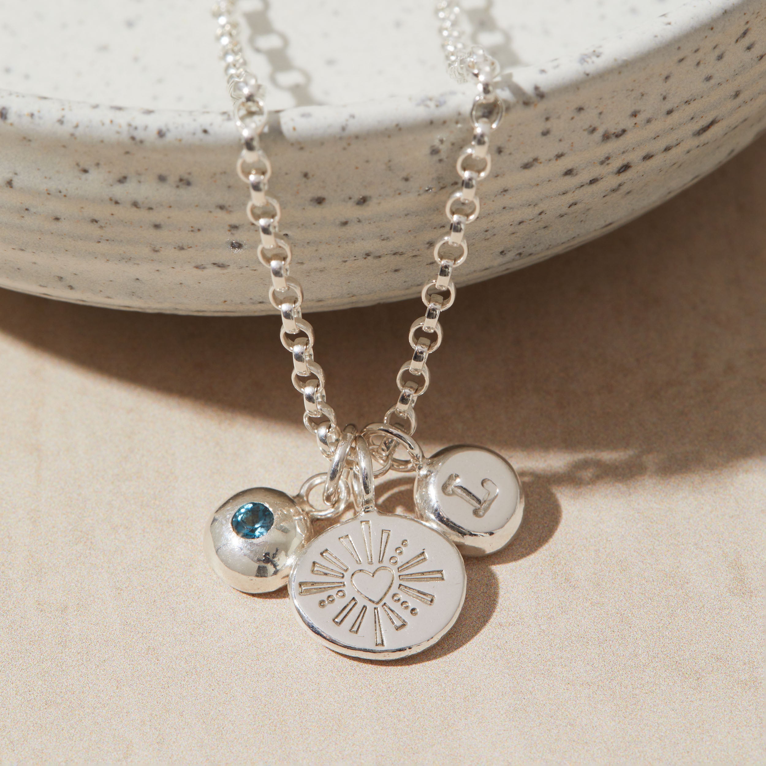 Silver necklace with heart, initial, birthstone charms on a beige surface