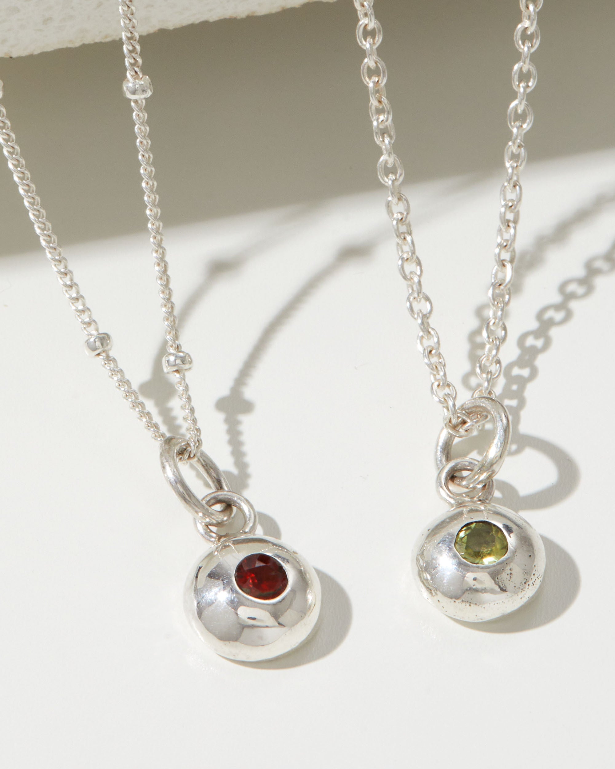 Two silver necklaces with gemstone pendants on a light background