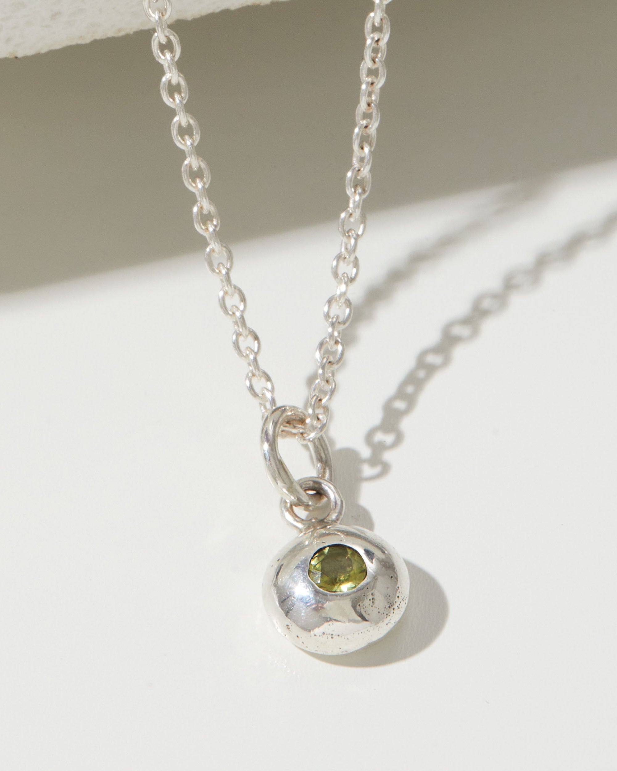 Silver necklace with a pendant featuring a green gemstone on a light background