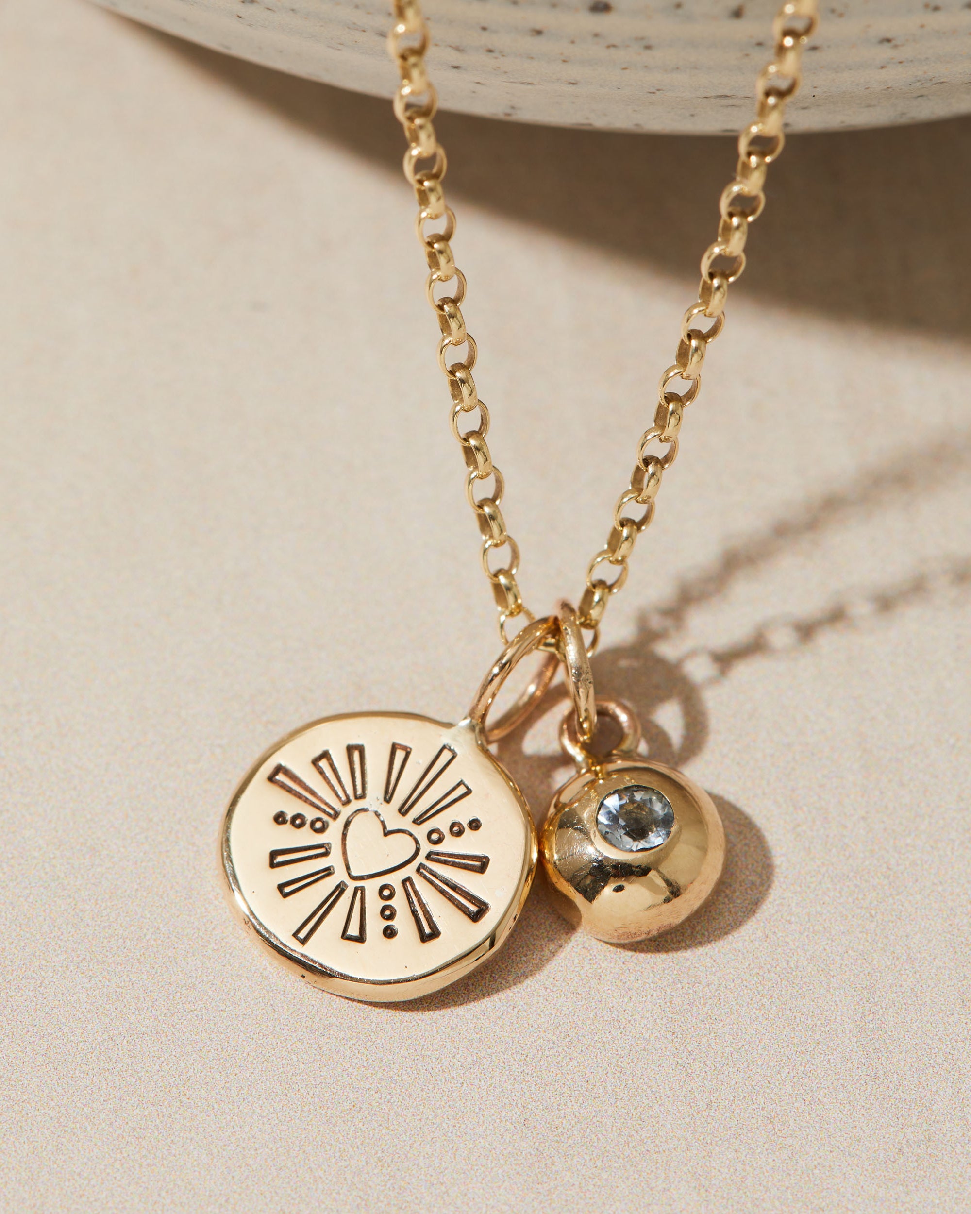 Gold necklace with heart and birthstone charms on a beige surface