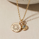 Gold necklace with heart and birthstone charms on a beige surface
