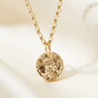 Gold necklace with a bark textured pendant on a soft beige background