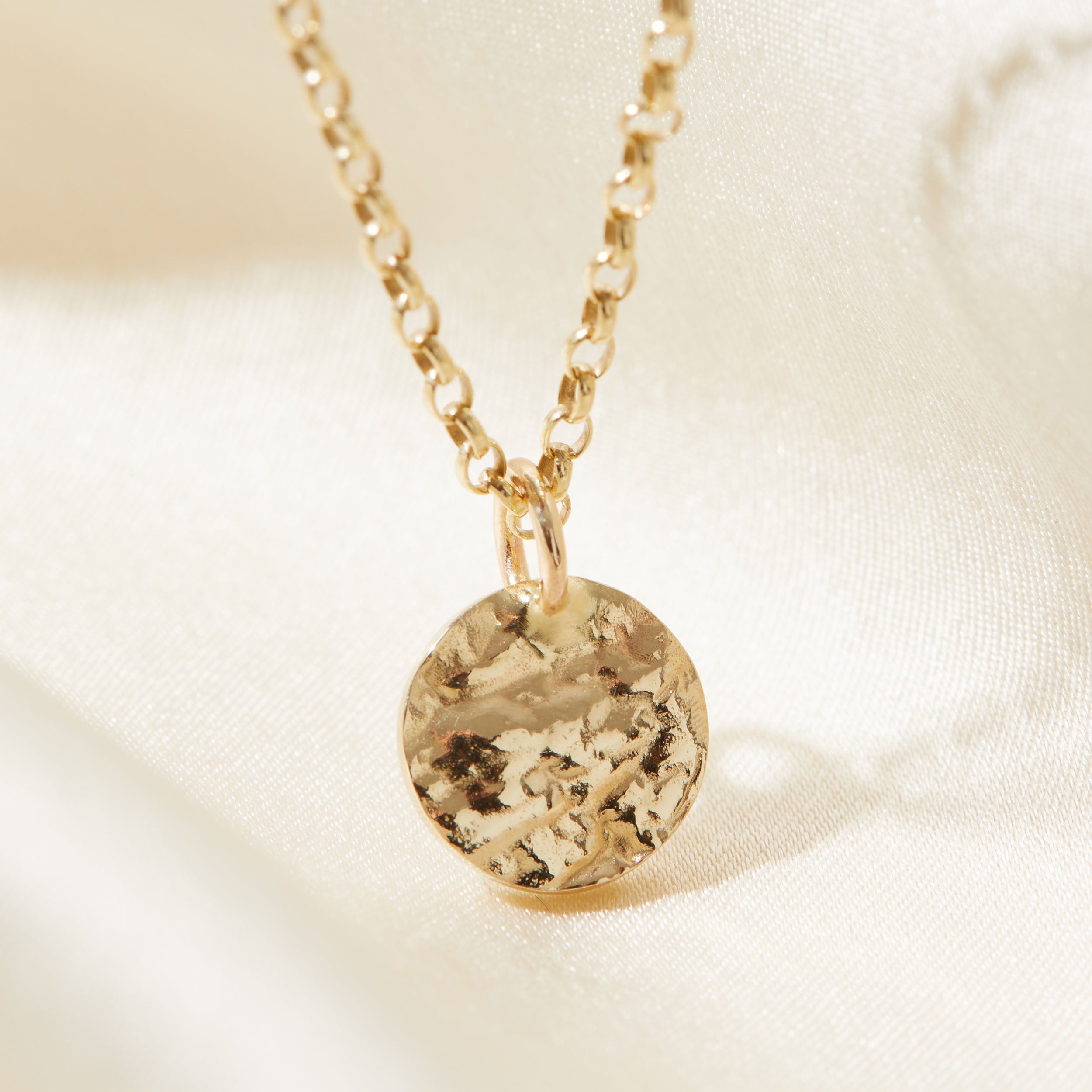 Gold necklace with a bark textured pendant on a soft beige background