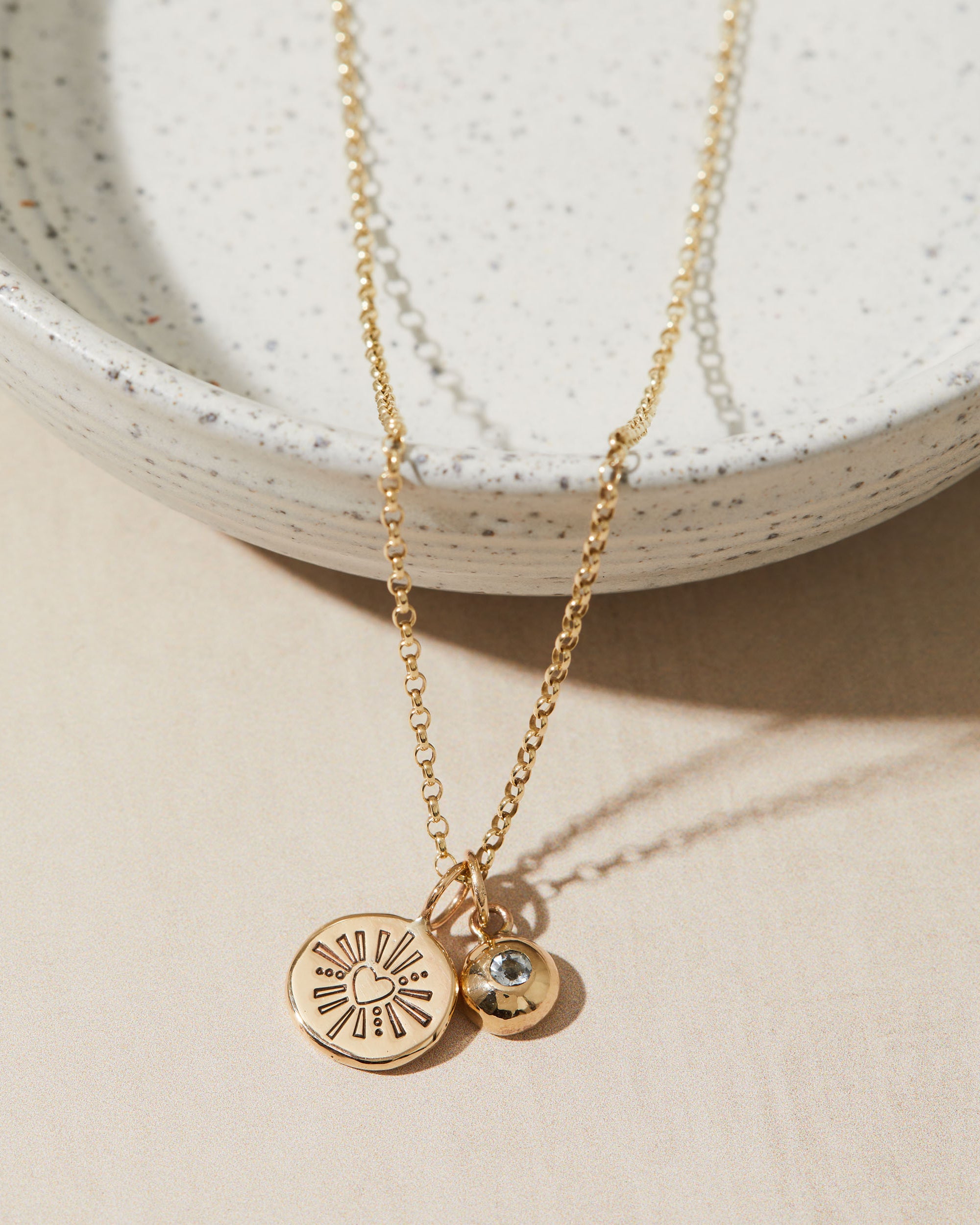 Gold necklace with birthstone and heart charms on a beige surface
