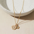 Gold necklace with birthstone and heart charms on a beige surface