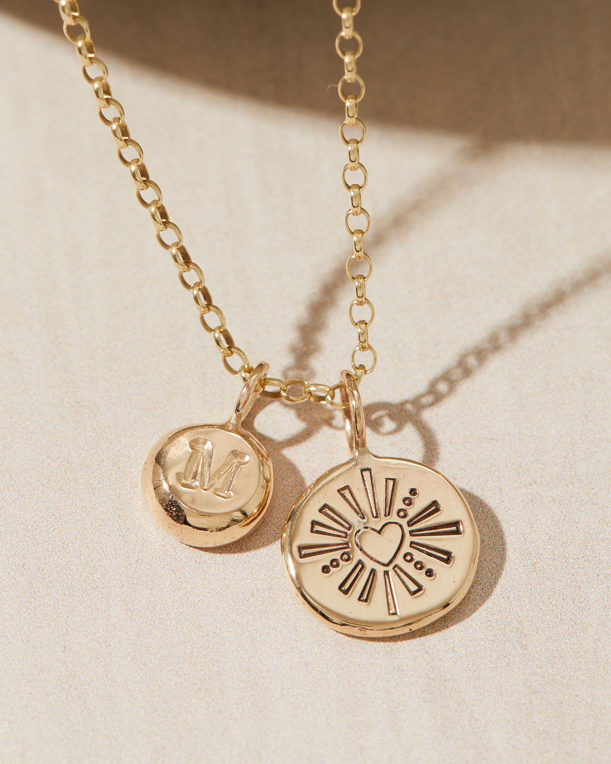Gold necklace with heart and initial pendants on a beige background