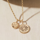 Gold necklace with heart and initial pendants on a beige background