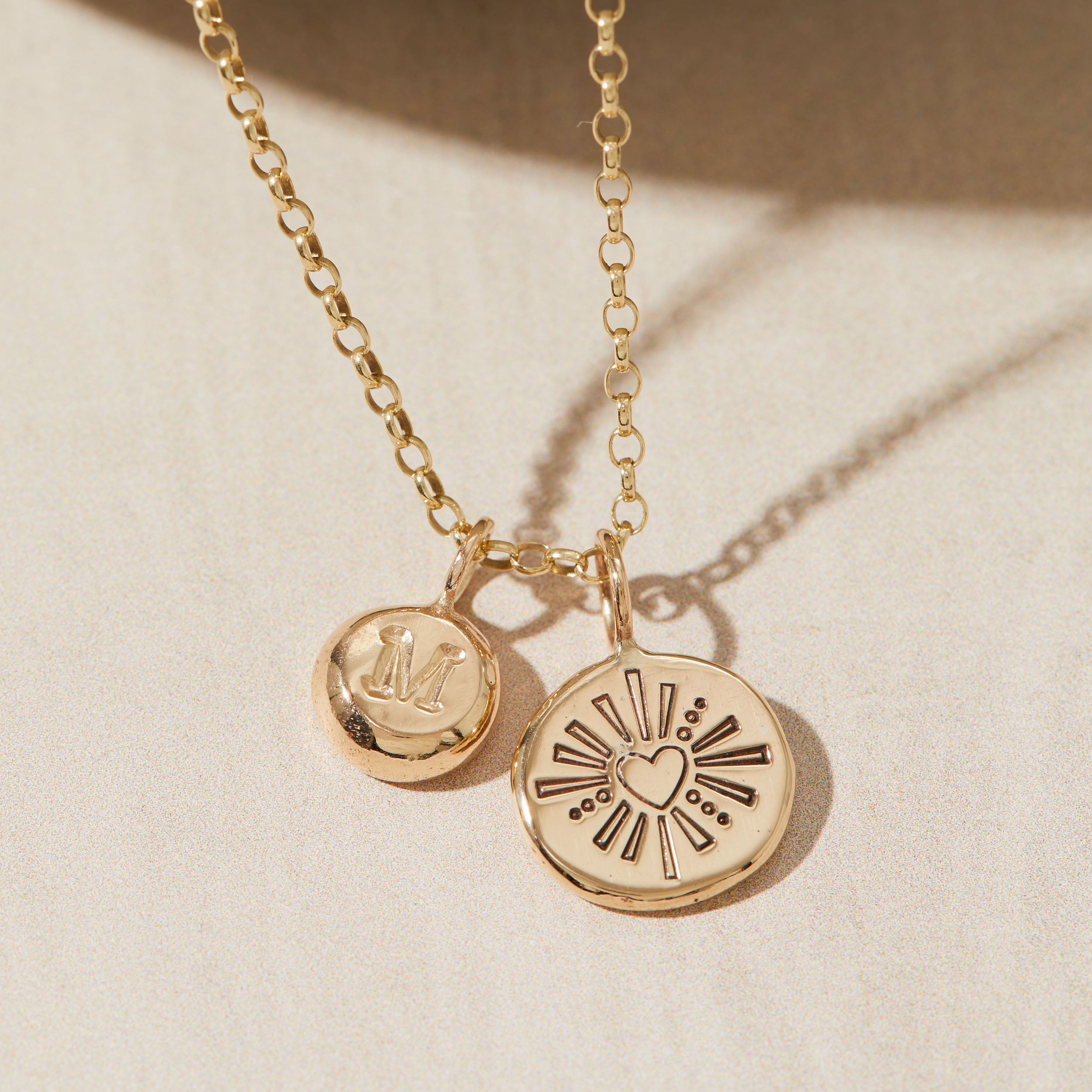 Gold necklace with heart and initial pendants on a beige background
