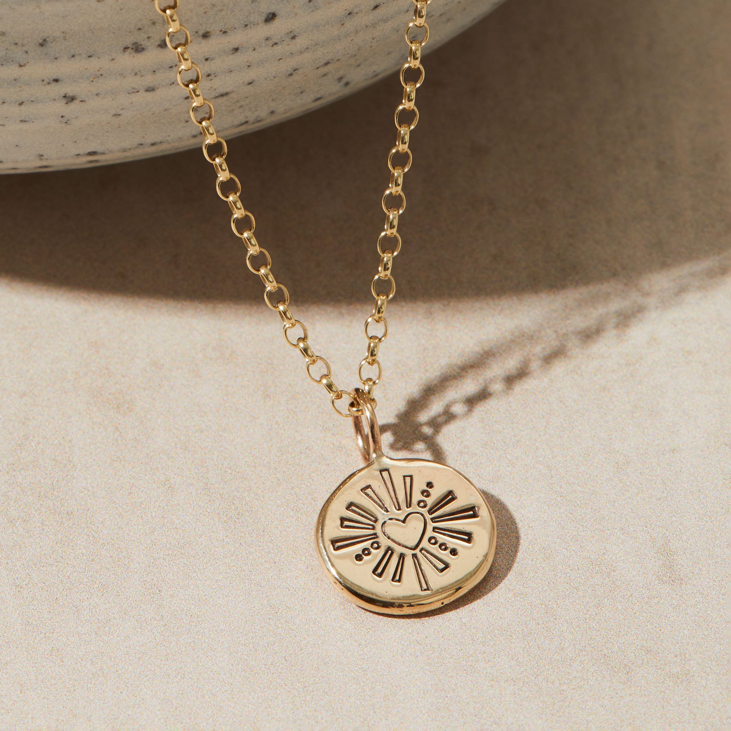 Gold necklace with a heart and sunburst pendant on a beige background